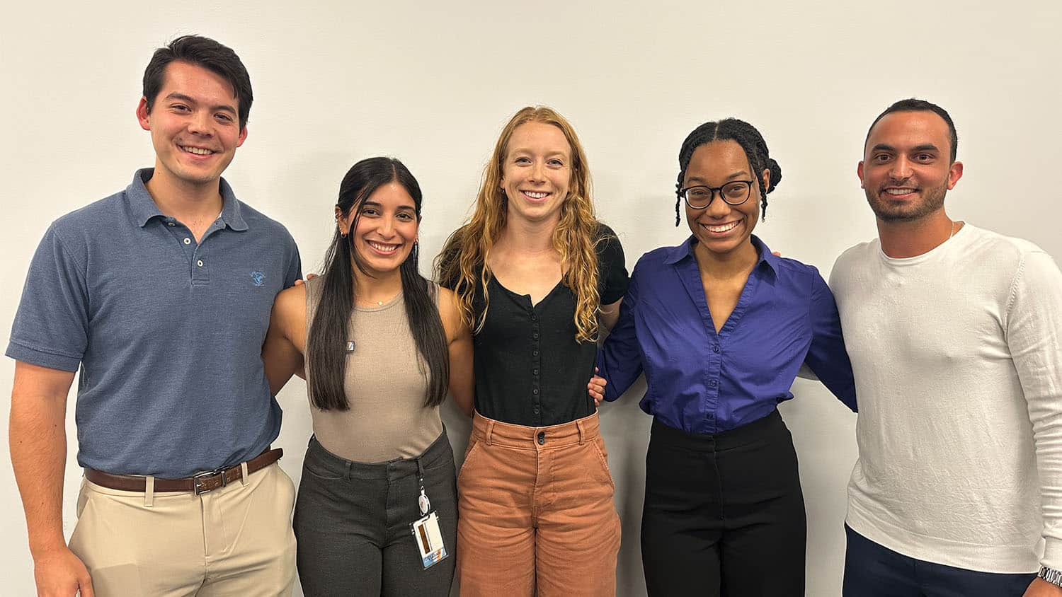 five alumni dressed in business casual attire stand with their arms around each other