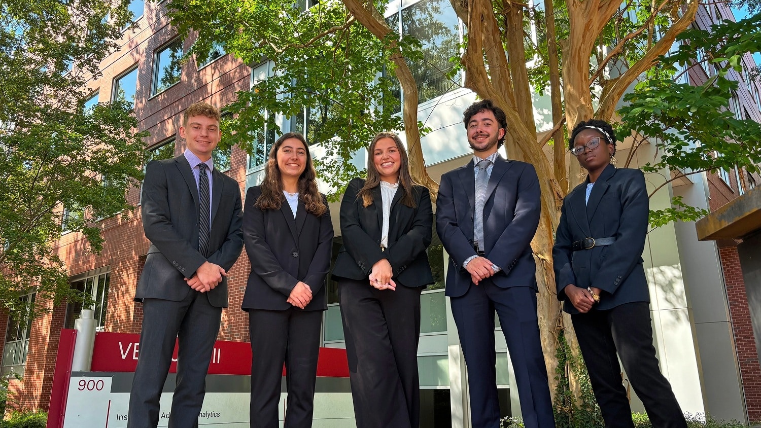 A group of five people in business attire standing outside a building for a group photo.